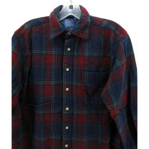 May include: A long-sleeve button-down shirt featuring a plaid pattern in shades of dark red, navy blue, and thin green lines. The shirt includes a standard collar, a single chest pocket on the left side, and light-colored buttons down the front placket.