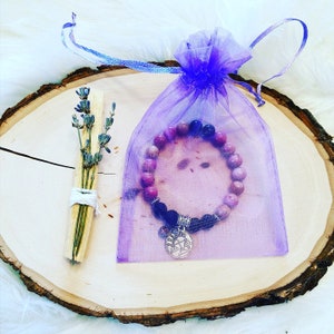May include: A purple and pink gemstone bracelet with a silver Libra charm, packaged in a purple organza bag with a lavender bundle.