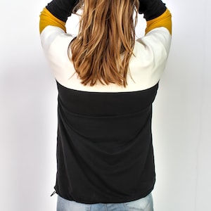 K&ouml;nnte beinhalten: Ein lang&auml;rmliges Shirt mit schwarzen, wei&szlig;en und gelben Streifen und einem Kordelzug am Saum.
