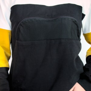 K&ouml;nnte beinhalten: Schwarzer Pullover mit einer gro&szlig;en Rei&szlig;verschlusstasche auf der Vorderseite. Die Tasche hat ein Mesh-Panel.