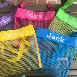 May include: Five colorful mesh tote bags with embroidered names: "Parker", "Grandma", "Colin", "Julian", and "Jack". Each bag features a different color trim and handle, including purple, pink, green, yellow, and blue. The bags are designed for carrying items.