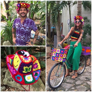 Może przedstawiać: Dwa kolorowe kapelusze na szydełku, jeden z symbolem pokoju i uśmiechniętą buzią, drugi z wzorem tęczy. Rower z koszykiem na szydełku i pokrowcem na siedzenie na szydełku.