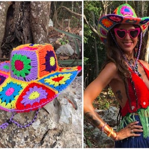 May include: A colorful, handmade crochet hat with a square crown and wide brim. The hat features a patchwork design with vibrant squares in shades of red, orange, yellow, green, blue, and purple. The hat has a chin strap.