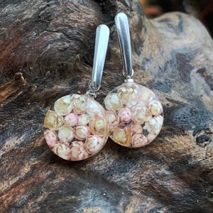 May include: A pair of silver earrings with round, clear resin charms filled with tiny pink and white flowers.