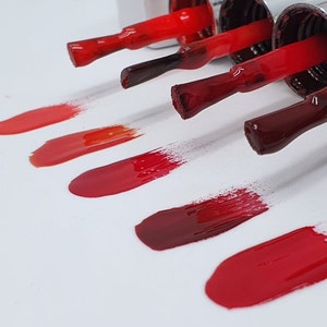 May include: Swatches of red nail polish in various shades, from light coral to deep burgundy, displayed on a white surface.