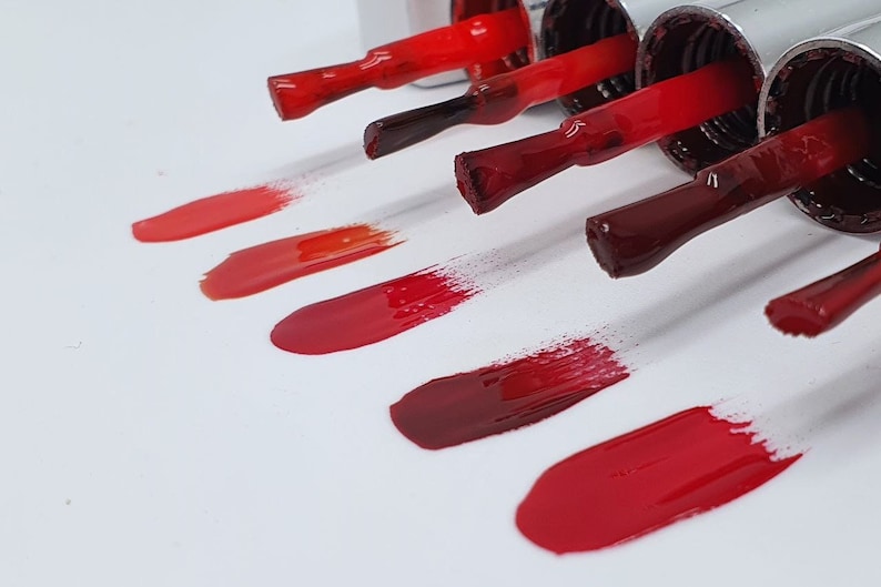 May include: Swatches of red nail polish in various shades, from light coral to deep burgundy, displayed on a white surface.