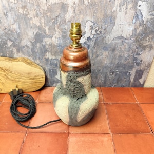 May include: A ceramic table lamp with a black, white and brown glaze. The lamp has a round base and a cylindrical shade. The lamp is wired with a black cord and plug.