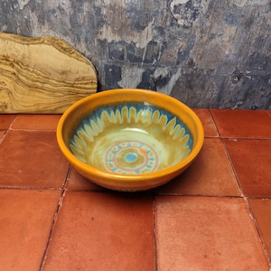 Könnte beinhalten: Eine Keramikschüssel mit einem gelben, blauen und orangen Design. Die Schüssel hat ein kreisförmiges Muster in der Mitte und ein wellenförmiges Muster am Rand.