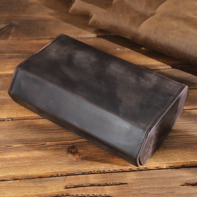 May include: A dark brown leather rectangular box with rounded edges. The box is made of a soft, supple leather and has a smooth, polished finish.