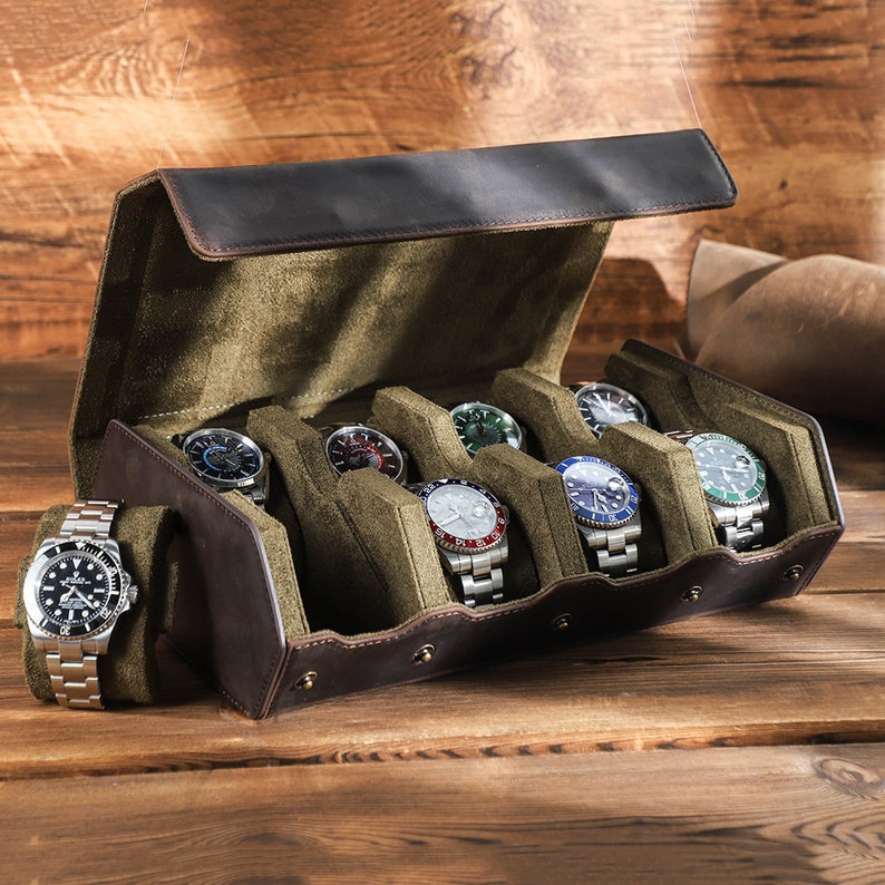 May include: A brown leather watch box with a green velvet interior. The box has six slots for watches and a hinged lid. The box is open and there are six watches inside.