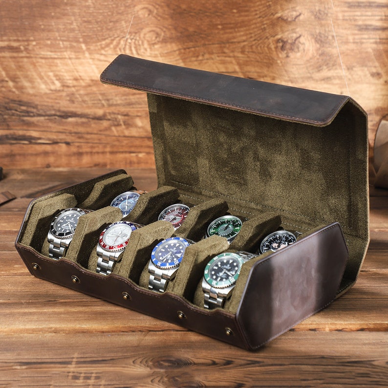 May include: A brown leather watch box with a green velvet interior. The box is open and has eight slots for watches. There are seven watches in the slots, each with a different colored face.