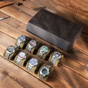 May include: A brown leather watch box with 10 watch slots, each with a green velvet cushion. The box is open and displays a variety of watches with different colored faces and bands.