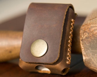 May include: A brown leather case with a brass button closure. The case has a stitched edge and is designed to hold small items.