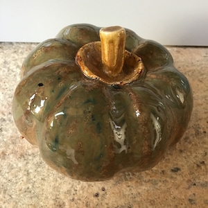 Può includere: Una zucca in ceramica con una glassa verde e marrone. La zucca ha un piccolo stelo rotondo.