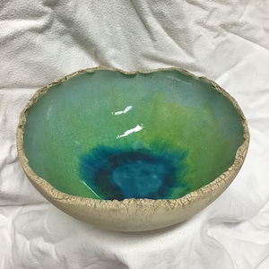 Könnte beinhalten: Eine große, ovale Keramikschüssel mit einer rauen, strukturierten Außenseite. Das Innere ist in Grün- und Blautönen glasiert, mit einem craquelé-Effekt.