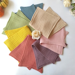 Peut inclure: Un ensemble de huit langes carr&eacute;s en tissu de diff&eacute;rentes couleurs, notamment vert, jaune, orange, rose et violet. Les langes sont dispos&eacute;s en cercle sur une surface blanche.