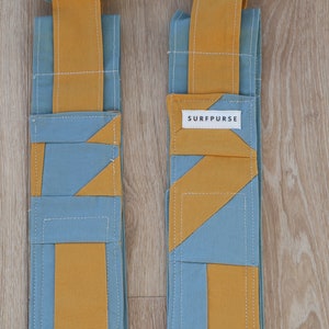 May include: Two long, narrow fabric pouches with a geometric pattern of blue and yellow. The pouch on the right has a label that reads "SURFPURSE".