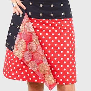 Può includere: Una gonna rossa con pois bianchi e una cintura nera con bottoni a pressione argentati. La gonna ha un lembo di tessuto fantasia che è ripiegato sul davanti. La gonna è etichettata "PACAP ORIGINAL".