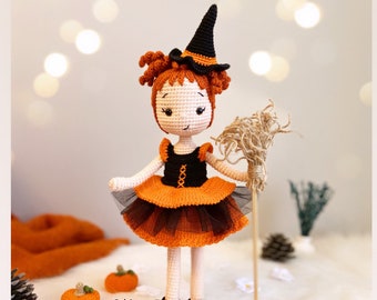 May include: A handmade crochet doll dressed as a witch, wearing a black hat with orange trim, a black bodice, and an orange and black tutu. The doll has red yarn hair and holds a broom. Small crochet pumpkins are in the foreground. The doll is approximately 10 inches tall.