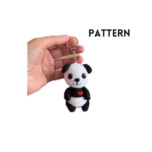 May include: A handmade crochet panda keychain with a silver keyring. The panda has a white body, black accents, and a red heart. The word "PATTERN" is printed in black.