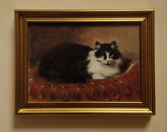 Puede incluir: Una pintura al óleo enmarcada de un gato blanco y negro con ojos verdes, acostado sobre un cojín con estampado rojo y dorado.