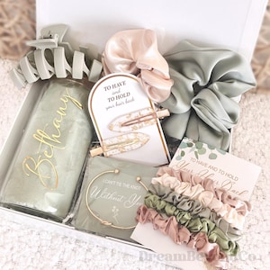 May include: A gift box filled with hair accessories, including a personalized water bottle, scrunchies, hair clips, and a bracelet. The box contains cards with the phrases "To Have and To Hold Your Hair Back" and "I Can't Tie The Knot Without You."