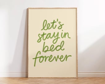 Könnte beinhalten: Gerahmter Druck mit den Worten "let's stay in bed forever" in grüner Schrift auf cremefarbenem Hintergrund. Der Rahmen hat eine helle Holzfarbe. Der Druck wird auf einem Holzboden angezeigt.
