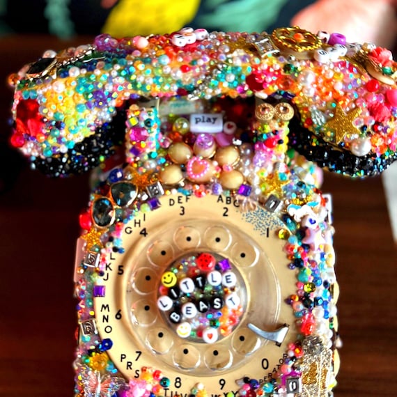 A fully bedazzled vintage rotary phone turned into a rhinestone objet d'art — absurdly extra, visually jaw-dropping, and genuinely handmade.