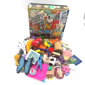 May include: A rectangular box with a collage cover featuring the text "box of WISHES" and a pile of assorted small objects including a blue butterfly, a pink hedgehog, a wooden spool, a blue clothespin, and a red Babybel cheese wax wrapper.
