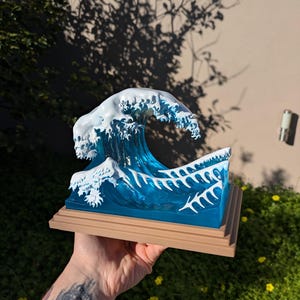 May include: A blue and white resin sculpture of a wave, reminiscent of the Great Wave off Kanagawa, on a wooden base.