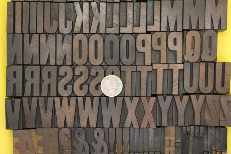 May include: A collection of wooden letterpress blocks in various sizes and styles, including uppercase letters, numbers, and punctuation marks. A silver coin is placed in the center of the image.