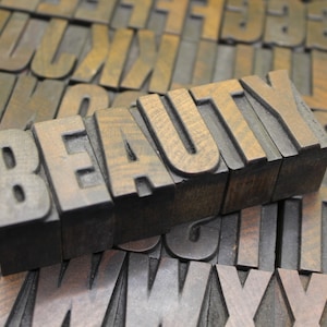 May include: The word "BEAUTY" spelled out in wooden letterpress blocks. The blocks are arranged in a row and are made of dark brown wood. The letters are raised and have a slightly worn appearance.