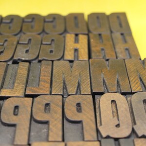 May include: A collection of wooden letter blocks in various sizes, including the letters G, C, H, L, M, P, and Q. The blocks are arranged in a staggered pattern, with the letters facing forward.