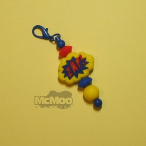 May include: A yellow and blue silicone keychain with a red and yellow "ZAP!" speech bubble charm. The keychain has a blue metal clip.