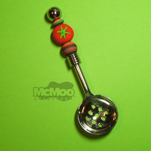 May include: A silver spoon with a decorative handle made of red, green, and orange beads. The spoon has a round, perforated bowl.