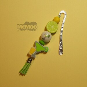 May include: Green, yellow, and white beaded bookmark with a silver metal bookmark tab. The beads feature a margarita glass, lime slices, and a green tassel. The bookmark has the text "McMoo Creations" on it.