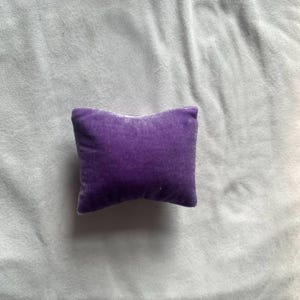 K&ouml;nnte beinhalten: Ein kleines, violettes Samtkissen. Das Kissen ist quadratisch und hat eine weiche, pl&uuml;schige Textur.