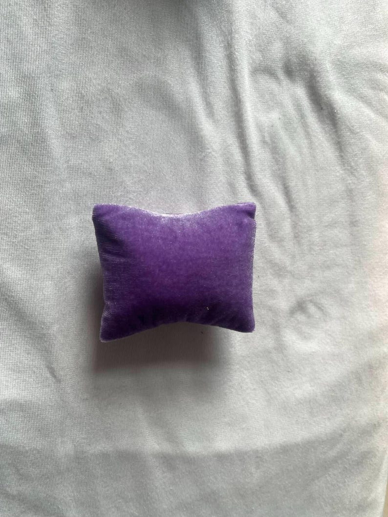 K&ouml;nnte beinhalten: Ein kleines, violettes Samtkissen. Das Kissen ist quadratisch und hat eine weiche, pl&uuml;schige Textur.