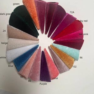 K&ouml;nnte beinhalten: Eine Farbkarte mit 12 Samtstoffproben in verschiedenen Farben, darunter Orange, Dunkelgr&uuml;n, Gr&uuml;n, Beige, Wei&szlig;, Blau, Koralle, Lila, Pink, Rubinrot und zwei Rosat&ouml;ne. Die Proben sind kreisf&ouml;rmig angeordnet und mit Zahlen beschriftet.
