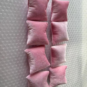 K&ouml;nnte beinhalten: Acht rosa Samtkissen, perfekt zum Ausstellen von Schmuck oder kleinen Gegenst&auml;nden. Die Kissen sind in zwei Reihen zu je vier angeordnet, wobei die obere Reihe leicht versetzt zur unteren Reihe ist.