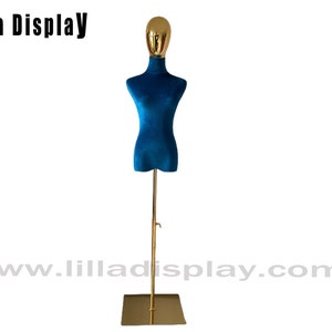 Könnte beinhalten: Eine blaue Samt-Torso-Schaufensterpuppe mit goldenem Kopf und Ständer. Der Ständer hat eine quadratische Basis und eine goldene Metallstange.