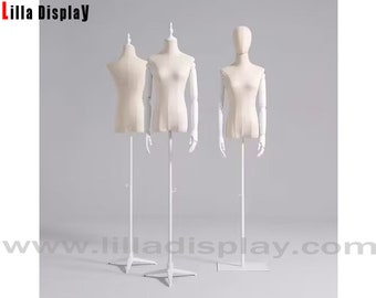 May include: Three white fabric mannequins with adjustable arms on white stands. The mannequins are headless and feature a torso and arms. The mannequins are used for displaying clothing.