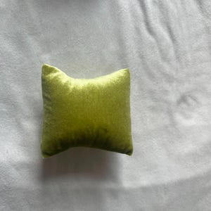 K&ouml;nnte beinhalten: Ein kleines, quadratisches Kissen mit weicher, samtiger Textur. Das Kissen ist in einem leuchtenden Limettengr&uuml;n.