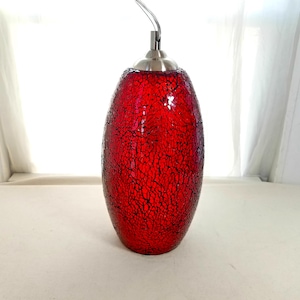 May include: A red mosaic glass pendant light with a crackle pattern. The light fixture has a teardrop shape and a brushed metal cap. The cord is silver. The light is hanging in front of a white background.
