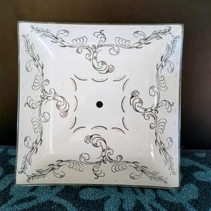 May include: Square white glass ceiling light cover with black scrollwork design. The cover has a central hole and a decorative border. The design features swirling lines and floral elements, creating an elegant, vintage aesthetic.