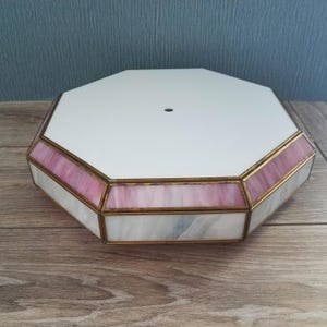 May include: An octagonal ceiling light fixture featuring a flat white top panel with a central hole. The sides are constructed from panels of pink and white marbled glass held together by a brass-toned metal frame, creating a geometric design.