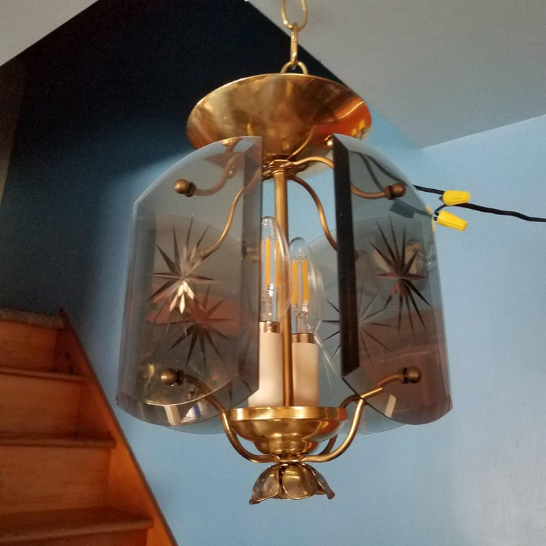 May include: Vintage brass chandelier with three light bulbs. The chandelier has a gold finish and features etched glass panels with starburst designs. The fixture is suspended from a chain and has a decorative floral base.