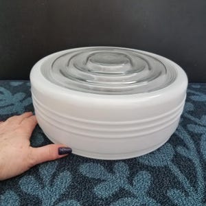 May include: A white, round light fixture with a clear glass center. The fixture has a series of horizontal ridges around the sides. The fixture is sitting on a blue patterned surface.