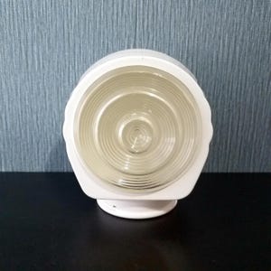 May include: A white, vintage-style light fixture with a clear, ribbed glass shade. The fixture has a rounded top and a square base. The glass shade is circular and has a spiral pattern. The fixture is designed to be mounted on a wall or ceiling.