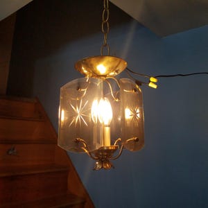 May include: Vintage brass chandelier with a clear glass shade. The shade features etched starburst designs. The fixture hangs from a chain and has a central light bulb. The chandelier is a classic lighting fixture.